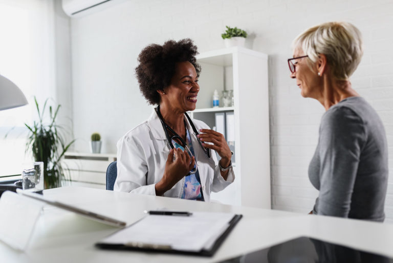 A female black ethnicity doctor sits at her office and examining elderly female patient