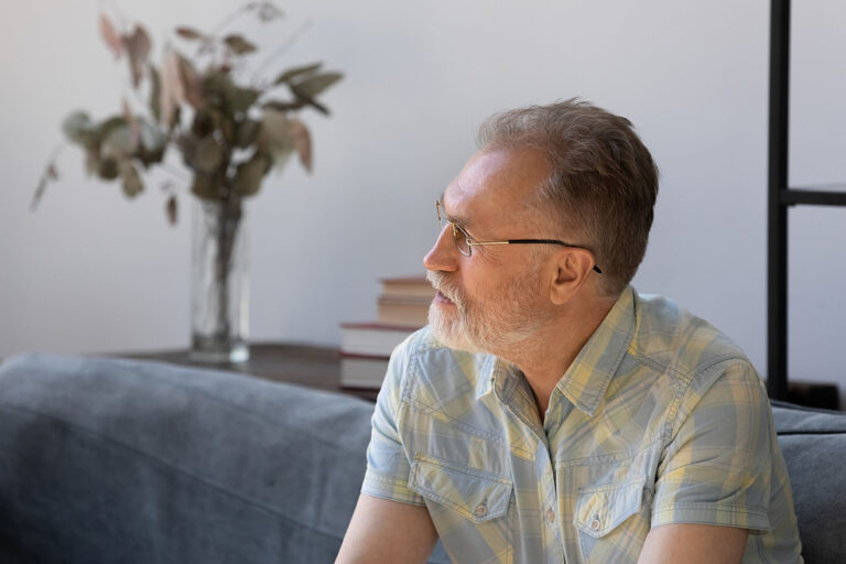 Thoughtful senior man making decision, sitting on couch at home, looking away, thinking with serious face. Sad pensive middle aged retiree, pensioner feeling lonely, anxious, depressed